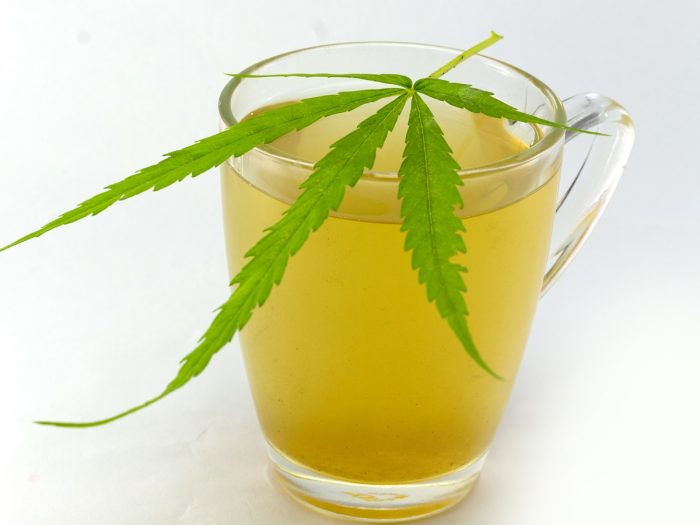 A cup of marijuana tea with fresh marijuana leaf placed on top